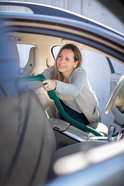 Hübsche Frau mittleren Alters staubsaugt den Innenraum eines Autos — Stockfoto