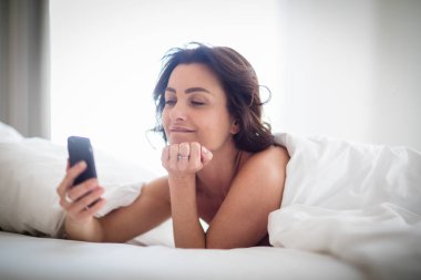Yatakta akıllı telefonunu kullanan güzel genç kadın