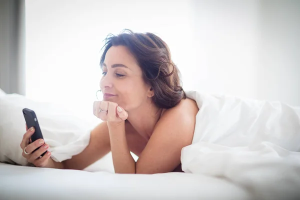 Krásná mladá žena, která používá svůj chytrý telefon v posteli — Stock fotografie