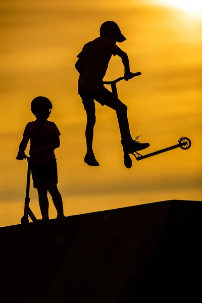 Silueta de niños pequeños montando scooters contra el fondo — Foto de Stock