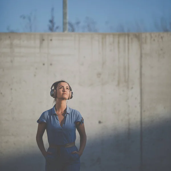 Csinos, fiatal nő fejhallgató álló betonfal ellen — Stock Fotó