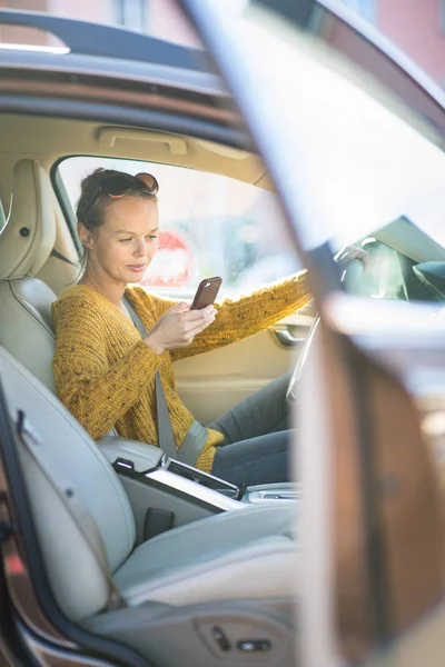 Mooie, jonge vrouw met behulp van haar slimme telefoon terwijl aan het stuur — Stockfoto
