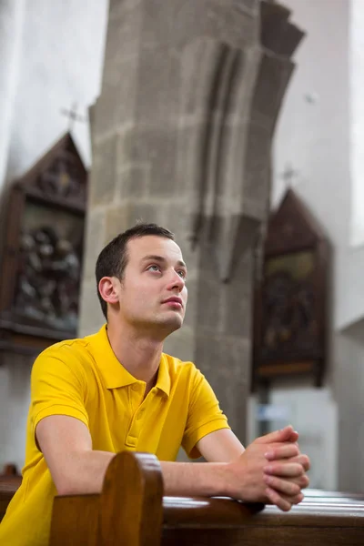 En stilig ung man som ber i en kyrka — Stockfoto