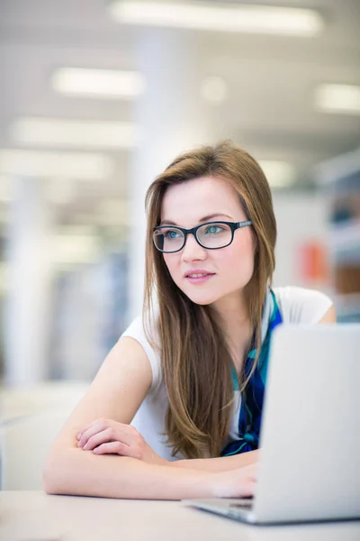 Mooie, vrouwelijke college student in een bibliotheek, op zoek naar een boek — Stockfoto