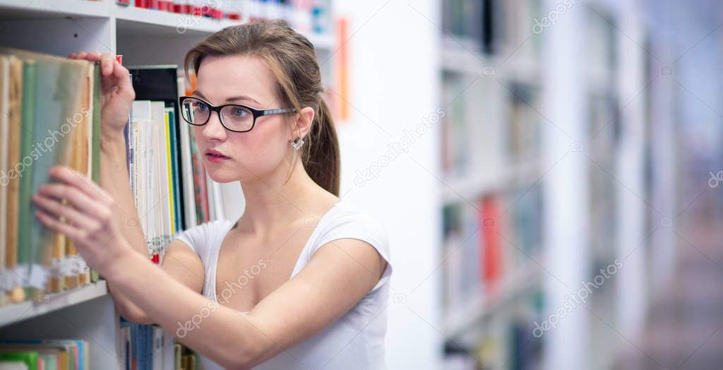 Pretty, female college student in a library, looking for a book 