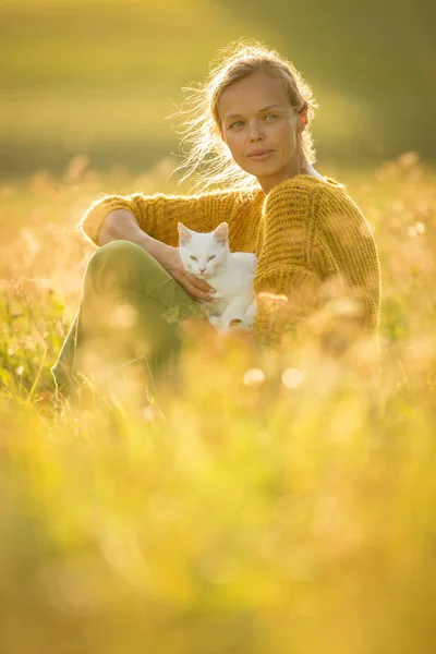 Güzel, genç bir kadın ve kedisi çimenlerde oturuyor. — Stok fotoğraf