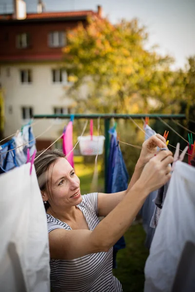 Jovem mulher colocando roupa em uma corda em seu jardim — Fotografia de Stock