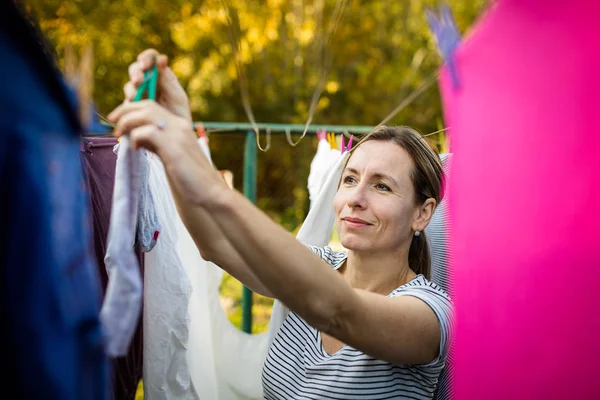 Jovem mulher colocando roupa em uma corda em seu jardim — Fotografia de Stock