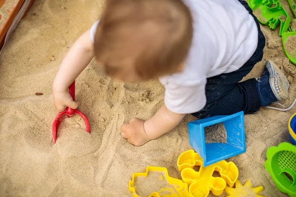 多くのプラスチックのおもちゃで砂の中で遊ぶ小さな子供 — ストック写真