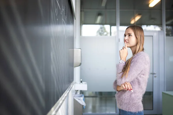 Söt, ung kvinnlig student framför en svart tavla under mattan — Stockfoto