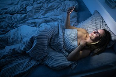 Yatakta cep telefonunu kullanan orta yaşlı güzel bir kadın. 