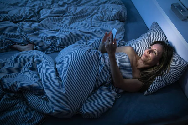 Ładna kobieta w średnim wieku używająca telefonu przed snem — Zdjęcie stockowe