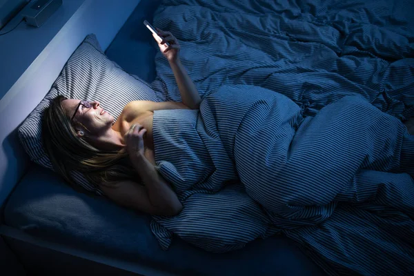 Csinos, középkorú nő használja a mobilját az ágyban. — Stock Fotó