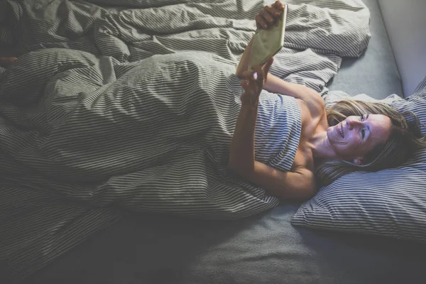 Bella, donna di mezza età utilizzando il suo computer tablet prima di dormire — Foto Stock