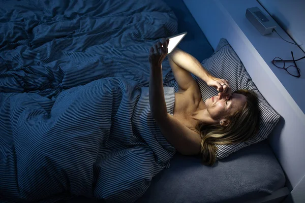 Mujer bonita y de mediana edad usando su teléfono celular en la cama — Foto de Stock