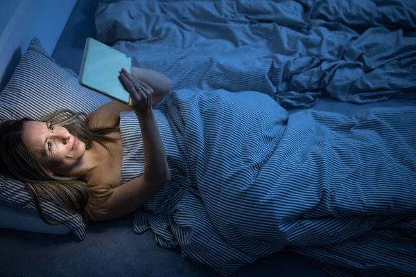 Όμορφη, μεσήλικη γυναίκα που χρησιμοποιεί το κινητό της στο κρεβάτι στο σπίτι — Φωτογραφία Αρχείου