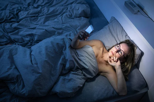 Hübsche Frau mittleren Alters, die ihr Handy zu Hause im Bett benutzt — Stockfoto