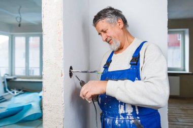 Yenilenmiş bir apartmanın elektrik tesisatında çalışan kıdemli bir adam.
