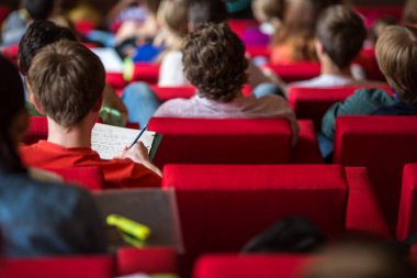 Üniversite öğrencileri sınıfta oturup notlar alıyorlar.