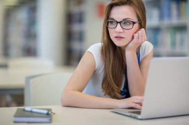 Kütüphanede bir kitap arayan güzel, bayan üniversite öğrencisi (sığ DOF; renk tonlu resim)