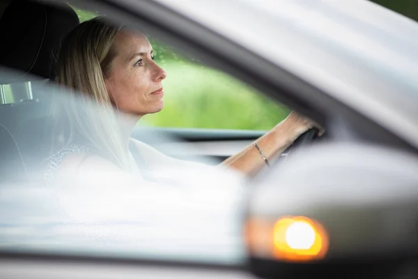 一个漂亮的中年妇女在开车上班的方向盘上 — 图库照片