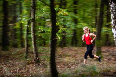 Güzelmiş. Genç bir kadın ormanda hızlı koşuyor. Hareket bulanıklığı tekniği hız ve hareket iletmek için kullanılıyor.