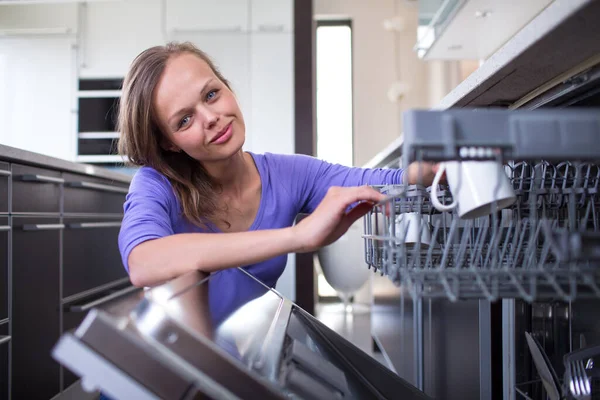 食器洗い機にカップを置く彼女の近代的で設備の整ったキッチンのかなり若い女性 彼女が家をきれいに保つのを助けるアプライアンス — ストック写真