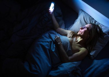 Güzel, orta yaşlı bir kadın uyumadan önce cep telefonunu evde kullanıyor.