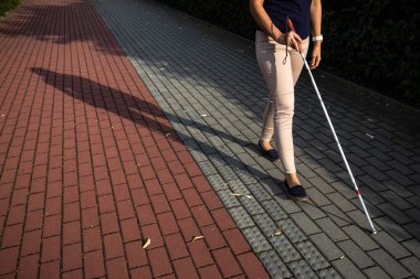 Beyaz bastonuyla sokaklarda yürüyen kör bir kadın.