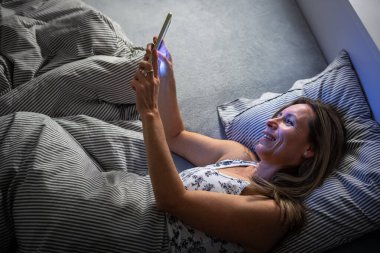 Güzel, orta yaşlı bir kadın akşamları yatmadan önce tabletini kullanıyor.