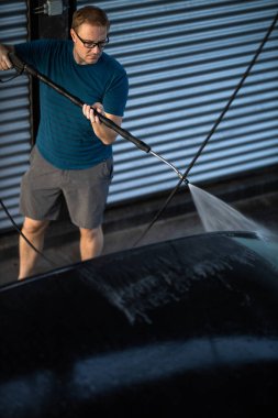 Genç adam herhangi bir hasarı önlemek ve detaylandırmak için sevgili arabasını manuel araba yıkamada dikkatlice yıkıyor.