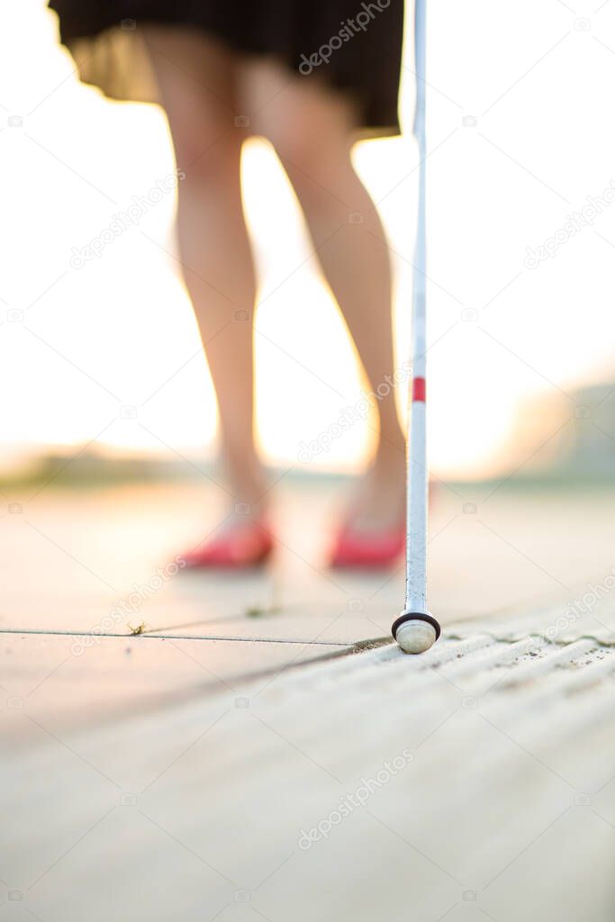 Blind woman walking on city streets, using her white cane to navigate the urban space better and to get to her destination safely