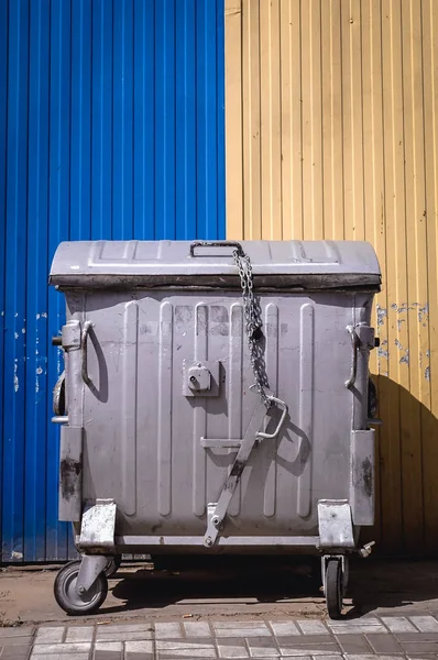 Large metal wheeled waste container on a yellow and blue background