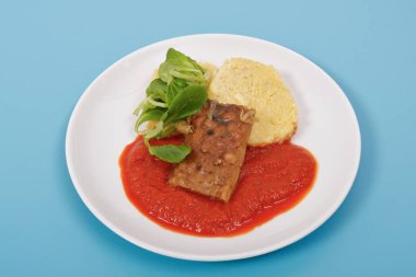 Tempeh domates sosu ve mavi bir arka plan üzerinde köfte ile