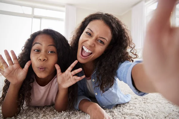 Mother And Daughter Lying On Rug And Posing For Selfie At Home