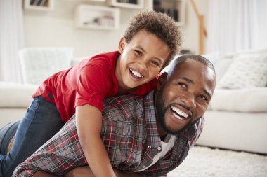 Son Climbing On Fathers Back, Playing Game In Lounge Together clipart