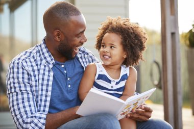 Young father and daughter reading book outside clipart