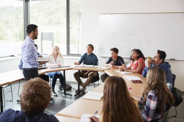 Male High School Tutor With Pupils Sitting At Table Teaching Maths Class clipart