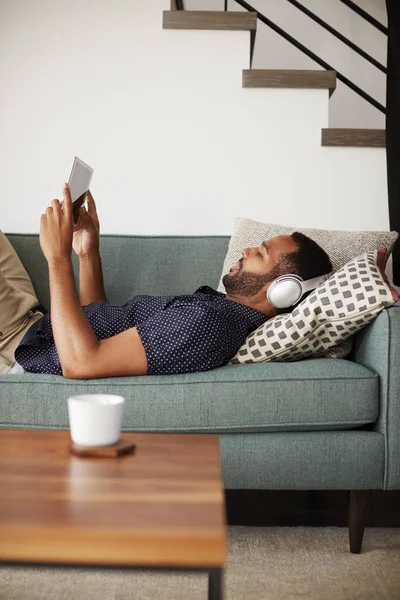 Hombre Acostado Sofá Casa Usando Auriculares Viendo Películas Tabletas Digitales — Foto de Stock