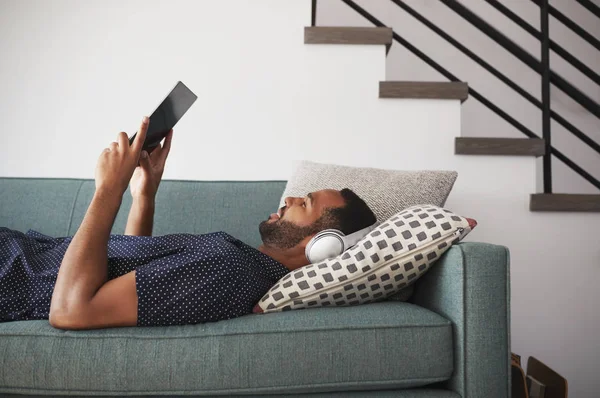 Hombre Acostado Sofá Casa Usando Auriculares Viendo Películas Tabletas Digitales — Foto de Stock