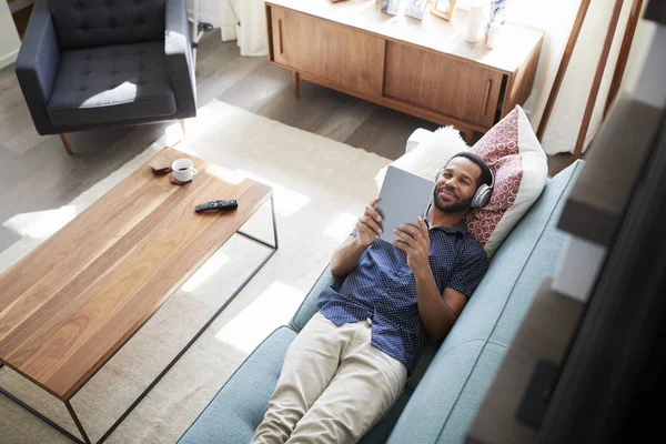 Man Ligger Soffan Hemma Bär Hörlurar Och Titta Film Digitala — Stockfoto