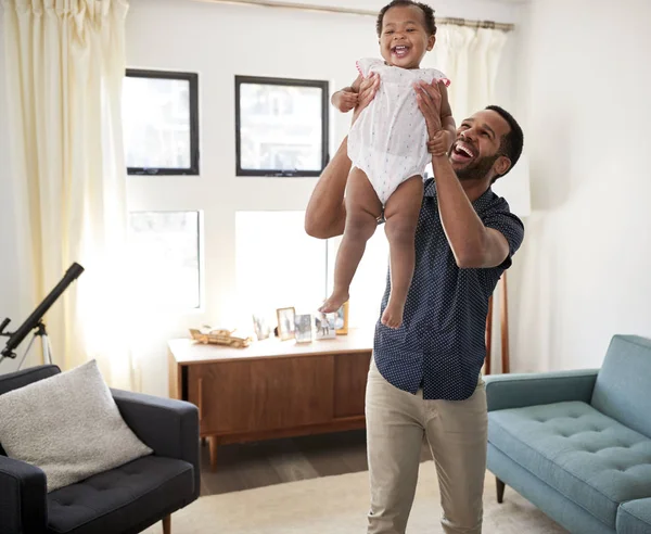 Father Standing In Lounge At Home Lifting Baby Daughter Into Air