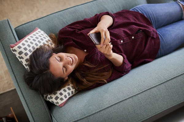Κάτοψη Της Ξαπλωμένη Στον Καναπέ Στο Σπίτι Χρησιμοποιώντας Κινητό Τηλέφωνο — Φωτογραφία Αρχείου