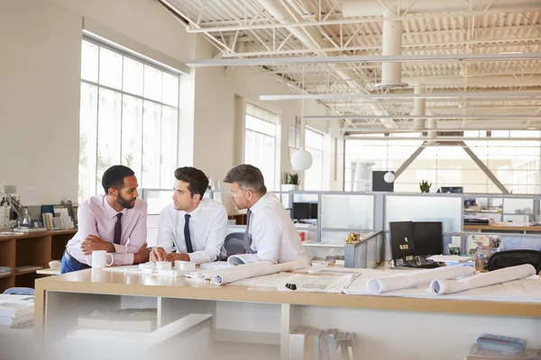 Three male architects in discussion in open plan office