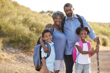 Grandparents With Grandchildren Wearing Backpacks Hiking In Countryside Together  clipart