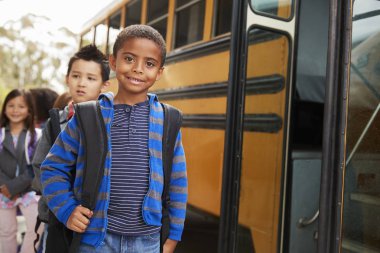 Young black schoolboy and friends wait to get on school bus clipart
