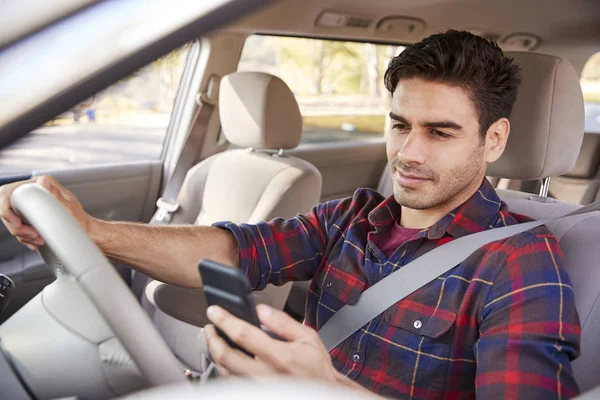 Young man in car checking smartphone while driving