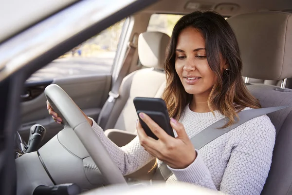 Młoda Kobieta Sprawdzanie Smartfona Podczas Jazdy Samochodem — Zdjęcie stockowe