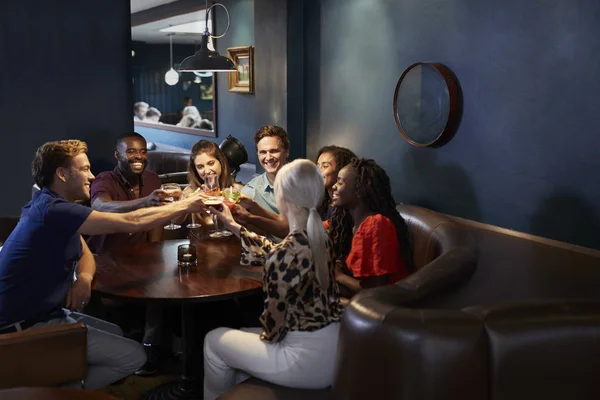 一群年轻的朋友围坐在桌旁 晚上在酒吧里做吐司 — 图库照片
