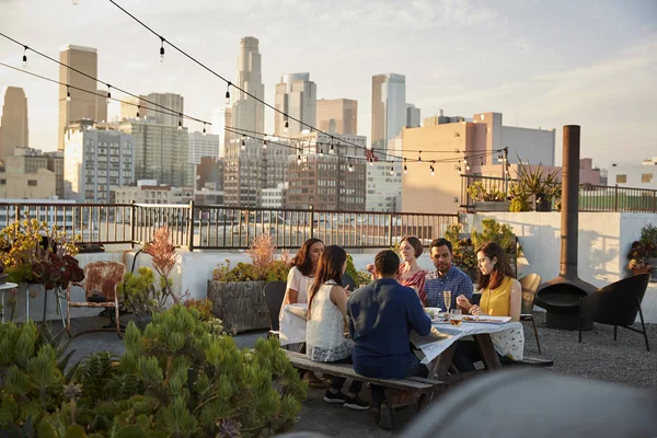 朋友聚集在屋顶露台用餐与城市天际线背景 — 图库照片